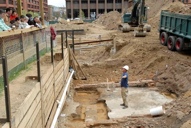 Visitors lean over a railing while an archaeologist speaks to them from the excavated foundations of the President’s House.